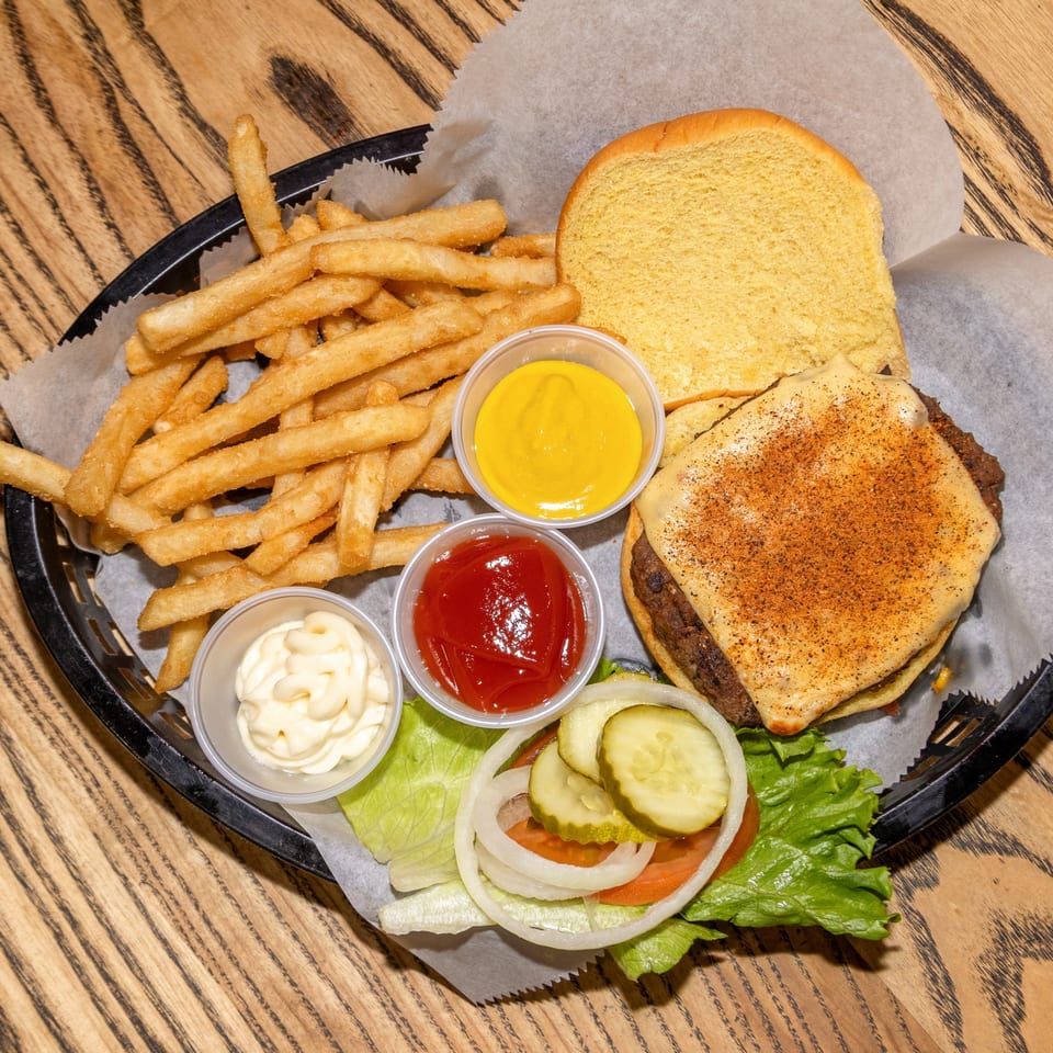 A Houligan's Corner cheeseburger with fries, ketchup, mustard, and mayonnaise in a basket.