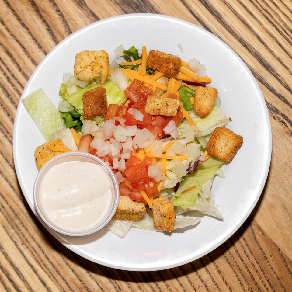 A fresh side salad with lettuce, diced tomatoes, onions, shredded cheese, croutons, and ranch dressing.