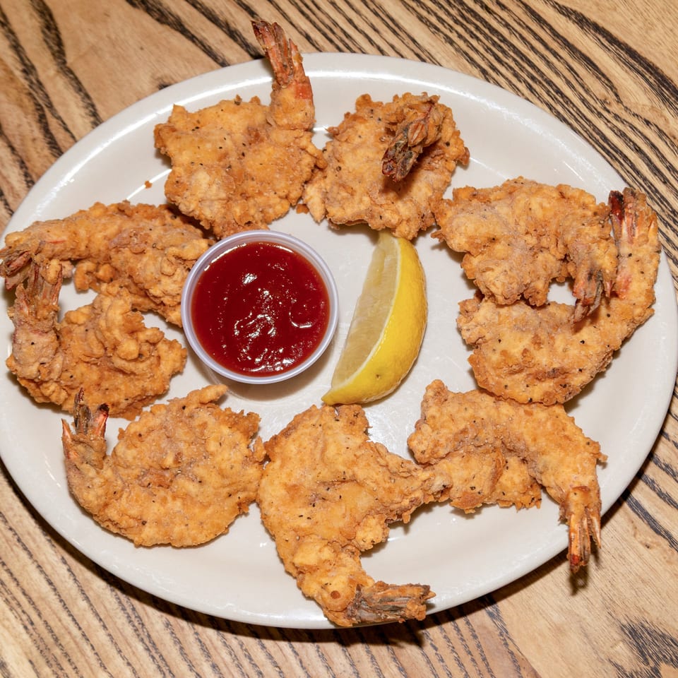 A plate of Houligan's Corner fried shrimp with cocktail sauce and a lemon wedge.