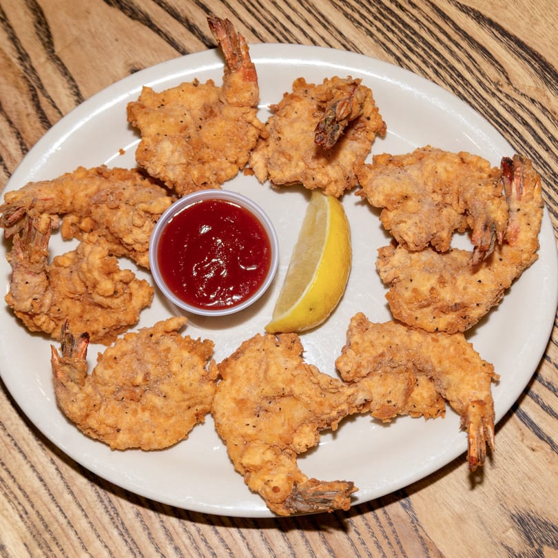 A plate of Houligan's Corner fried shrimp with cocktail sauce and a lemon wedge.