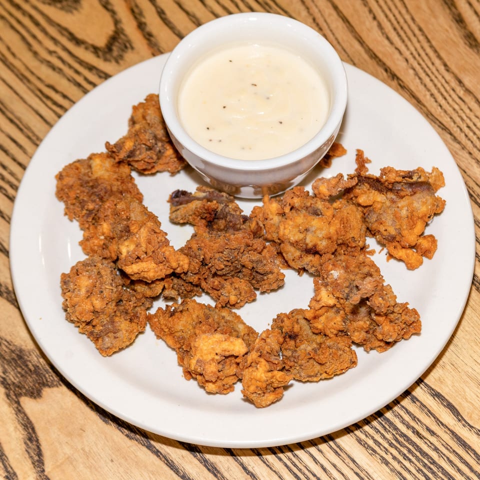 Houligan's Corner fried oysters, golden brown and crispy, served with a side of creamy white sauce.
