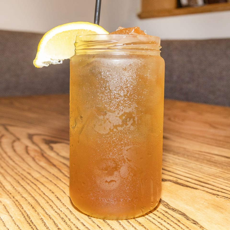 Iced tea in a mason jar with a lemon slice and straw on a wooden table.