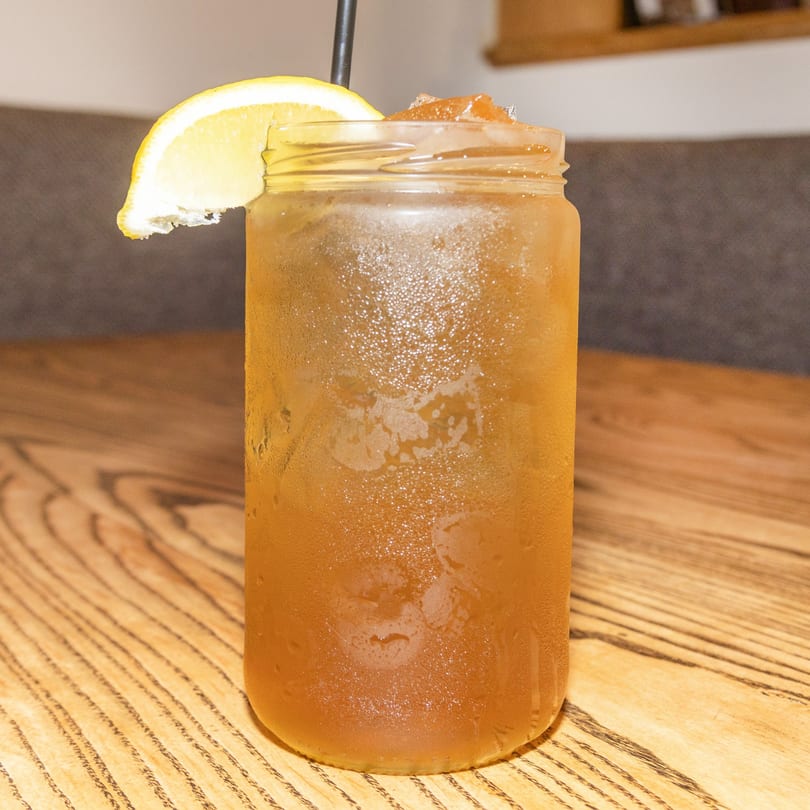 Iced tea in a mason jar with a lemon slice and straw on a wooden table.