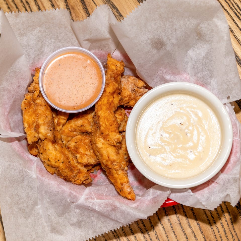 Crispy Houligan's Corner chicken tenders in a red basket with two dipping sauces.